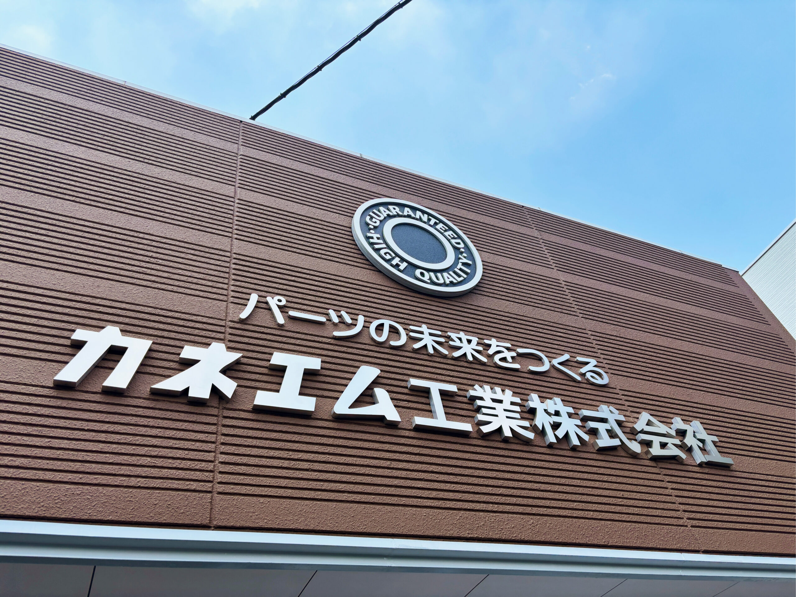 社名・キャッチコピー・円形エンブレムを組み合わせた外壁サインの近景